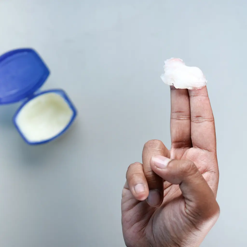 Petroleum jelly in an open jar with a sample on fingertips.