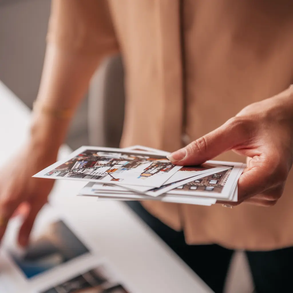 Hands arranging small printed photographs above a work table.