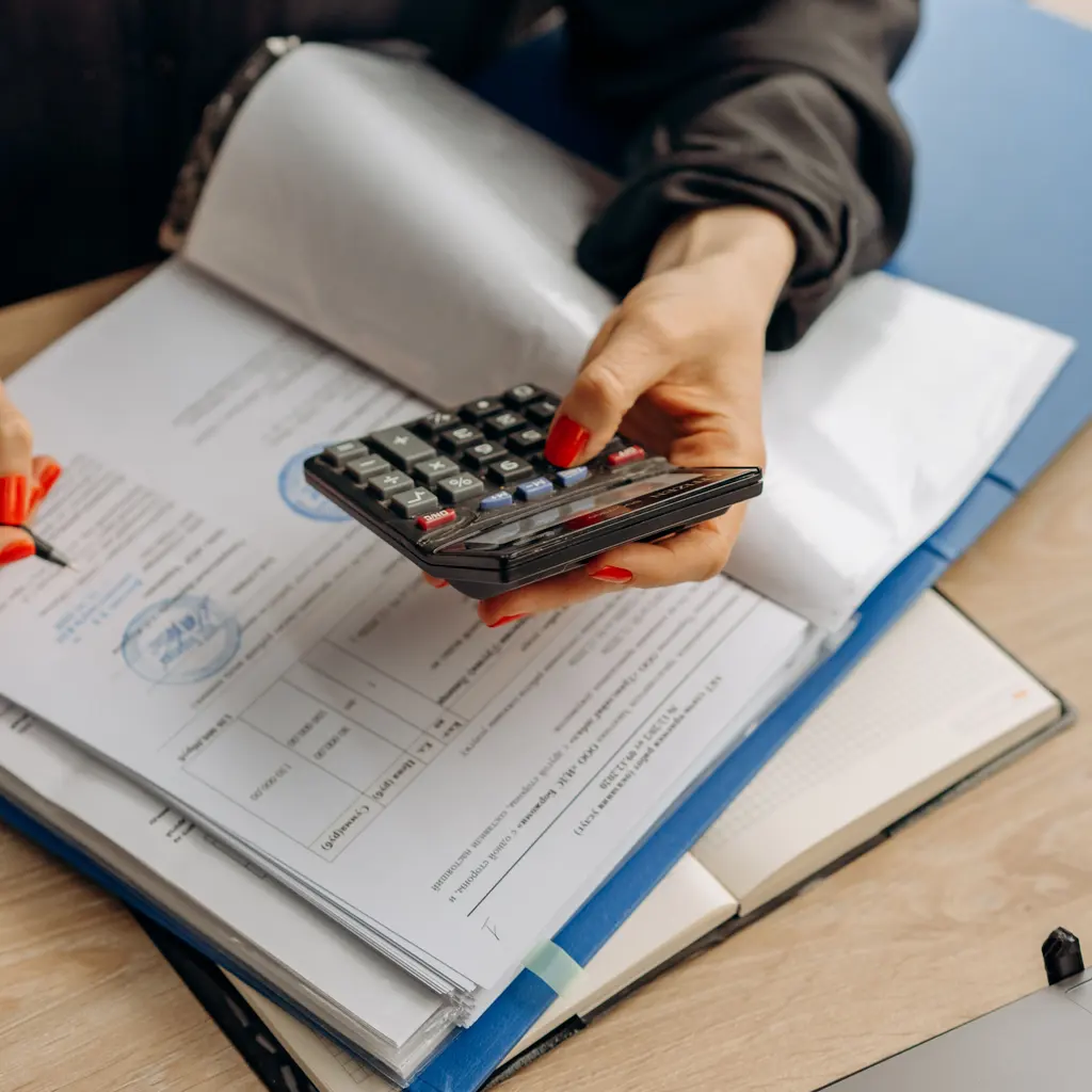 Hands using a calculator over forms and an open binder.