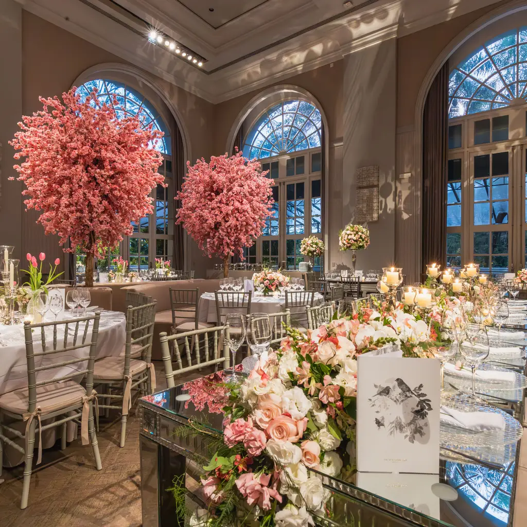 Reception tables set with glassware and flowers beneath large pink floral arrangements.