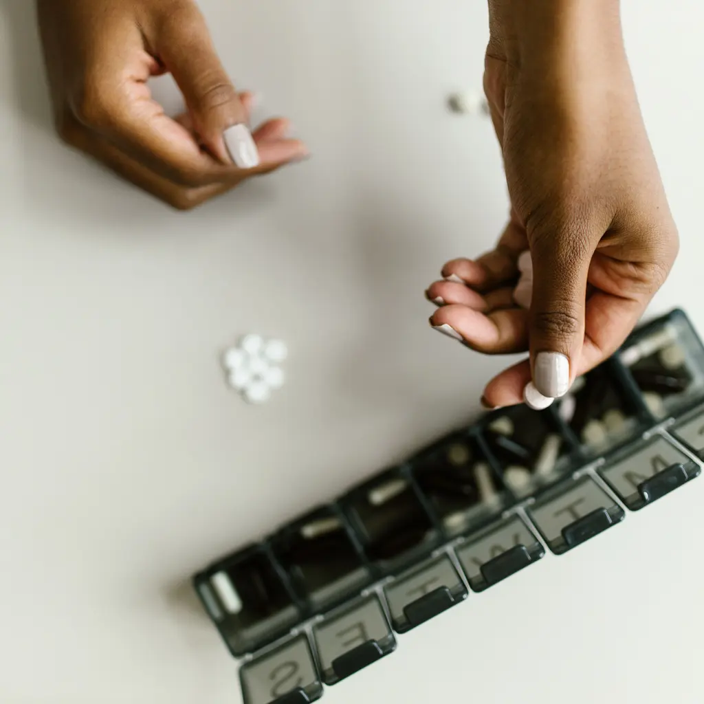 Hands organizing tablets in a weekly medication box.