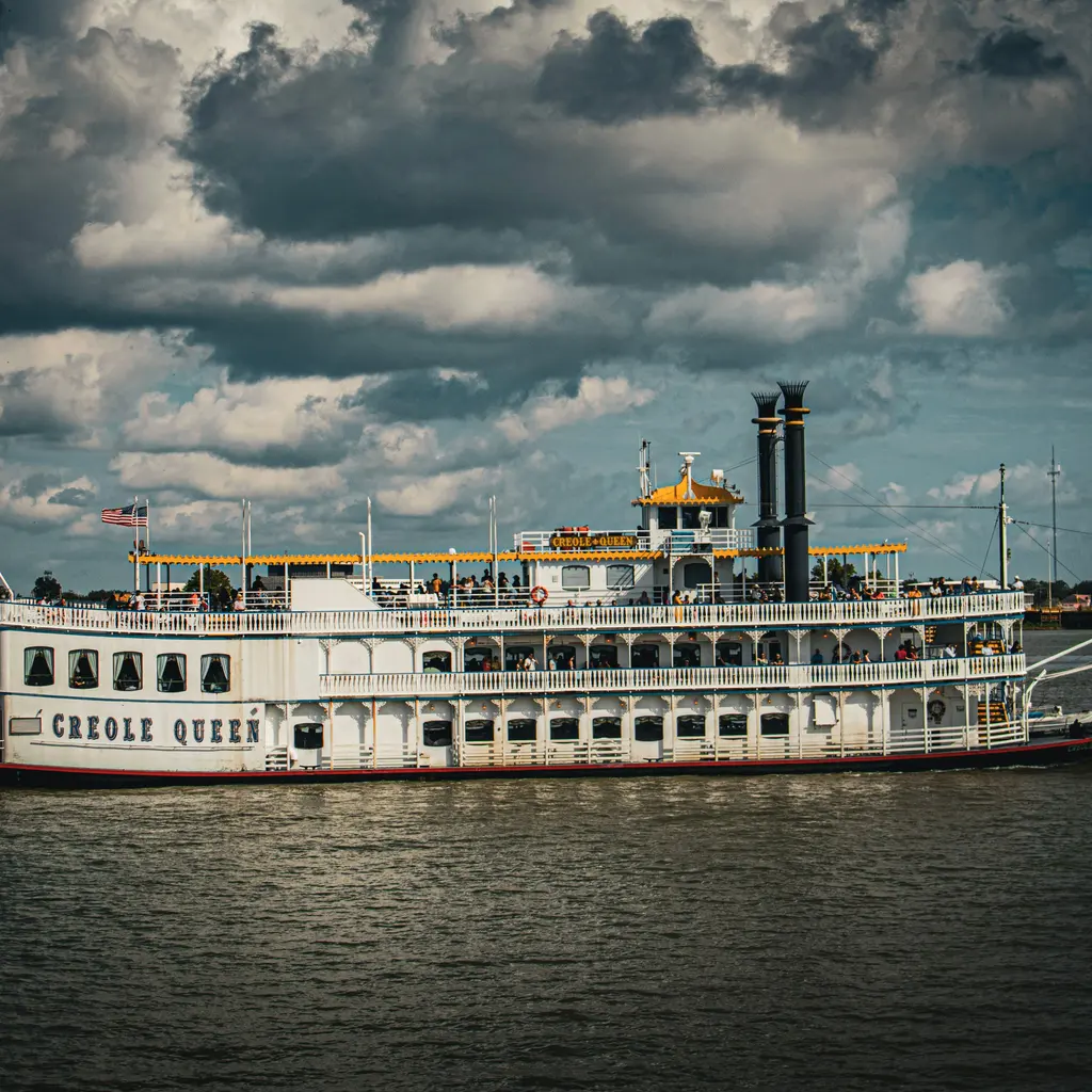 A paddlewheel passenger riverboat with multiple decks traveling on a river.