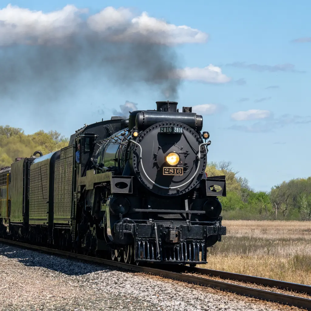 A restored steam locomotive pulling passenger coaches through open countryside.
