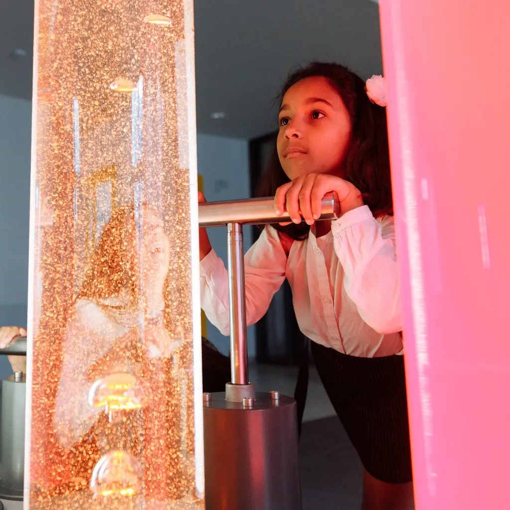 A young visitor using a hands-on exhibit beside an illuminated bubble column.