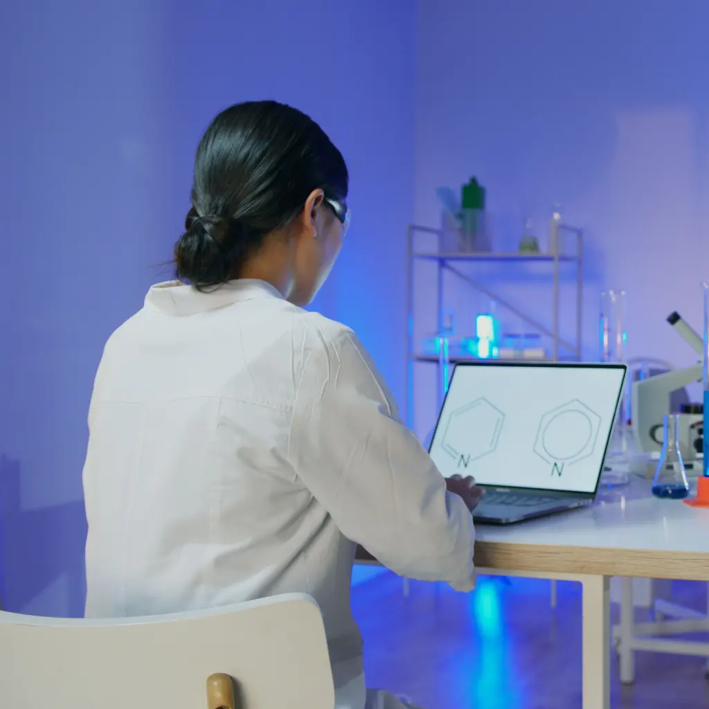 A lab-coated professional reviewing molecular diagrams on a laptop.
