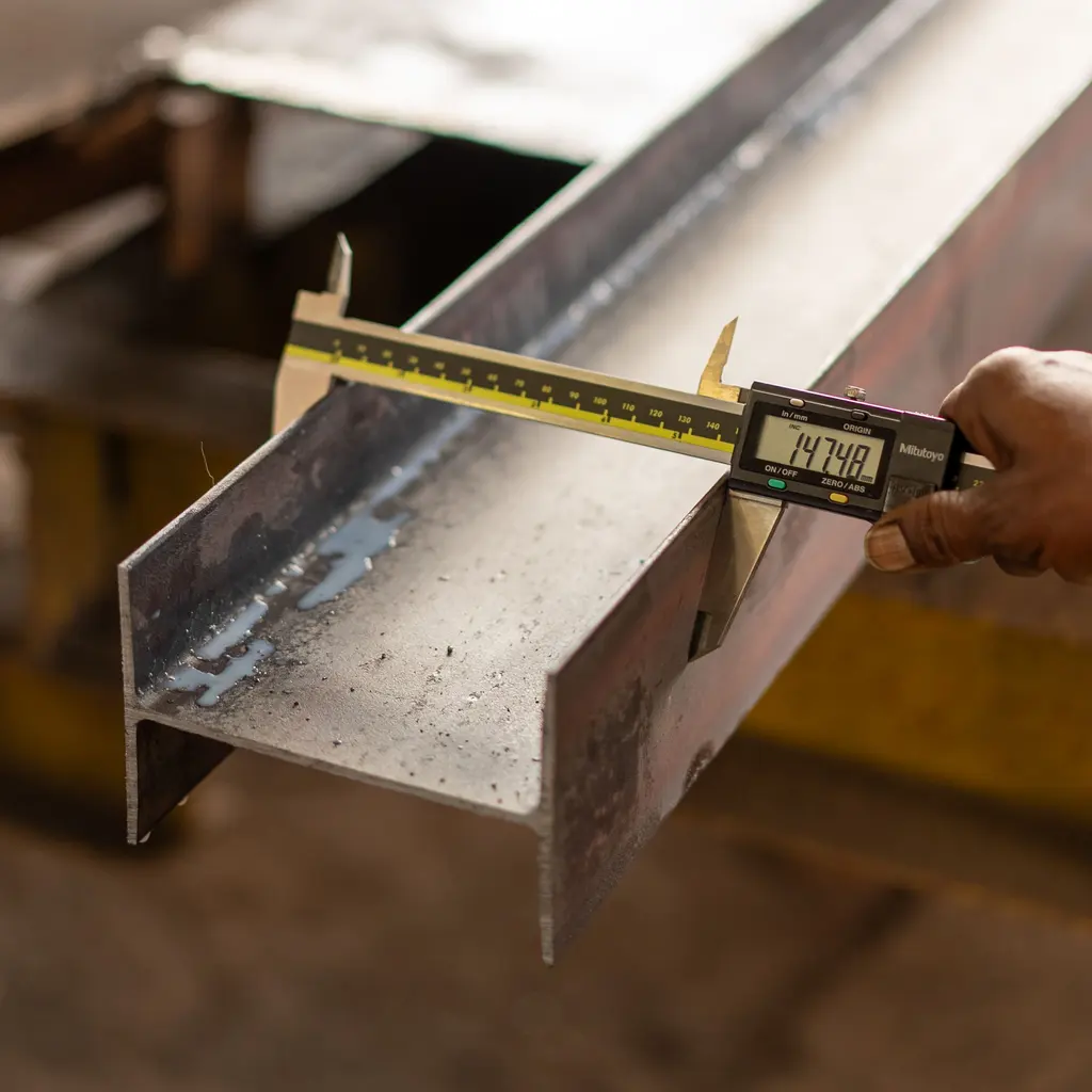 Hands using a digital caliper to measure the width of a steel section.