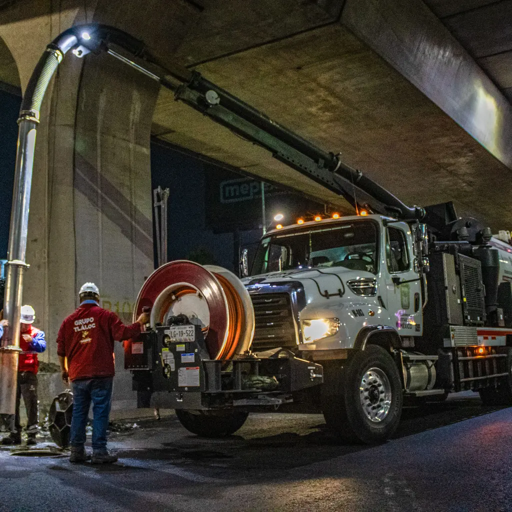 A vacuum service truck and crew working with a suction boom at night.