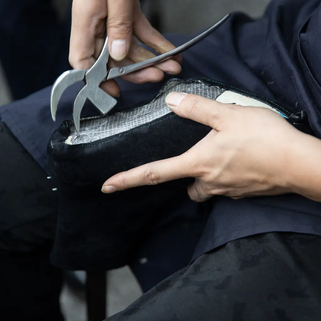 Hands working on a leather shoe with cobbler’s pliers.