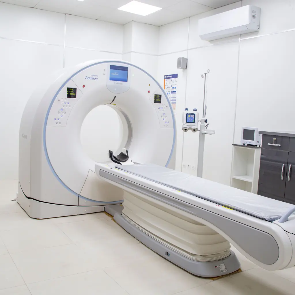 An empty CT scanning room with a patient table and imaging gantry.