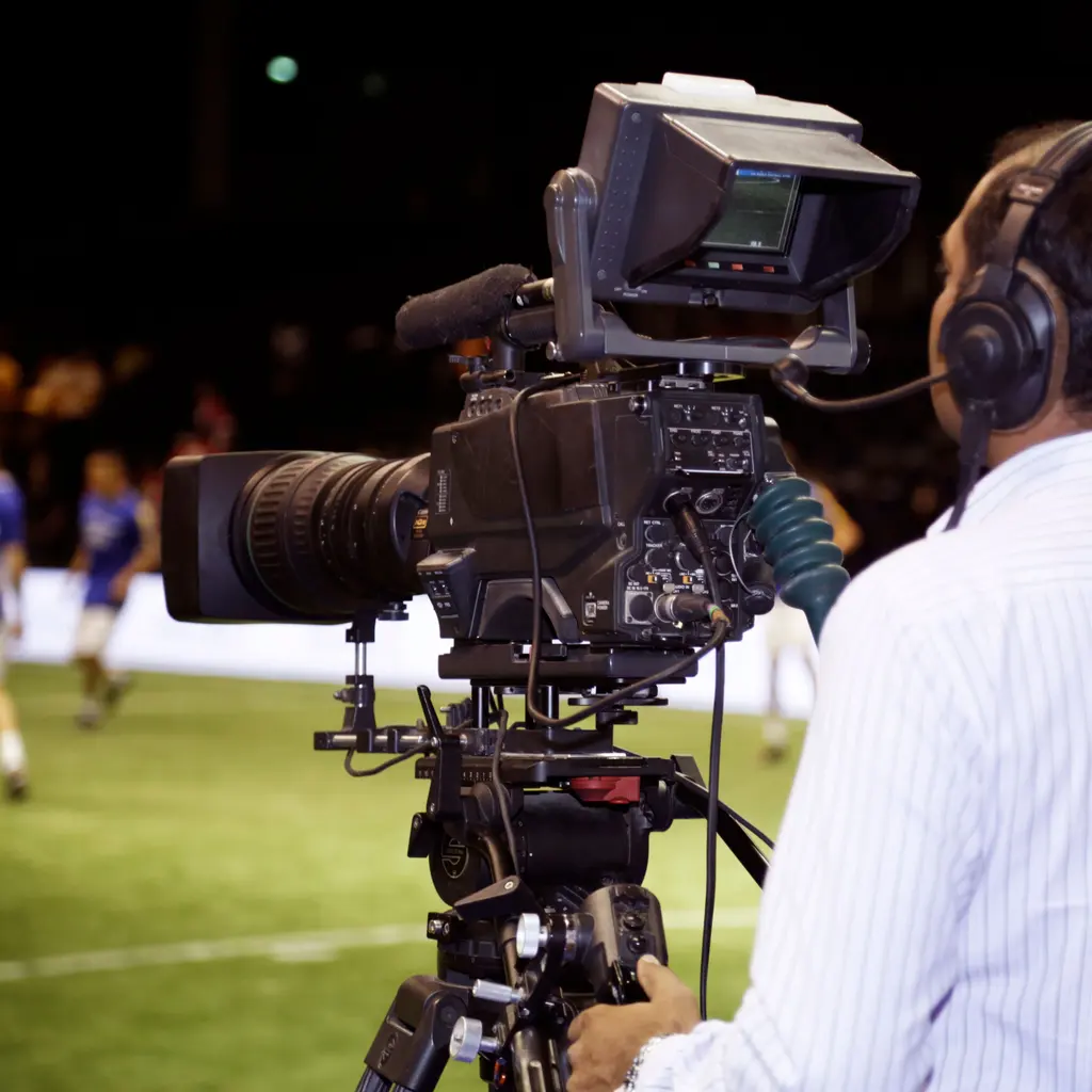 A television camera operator filming a soccer match from beside the field.