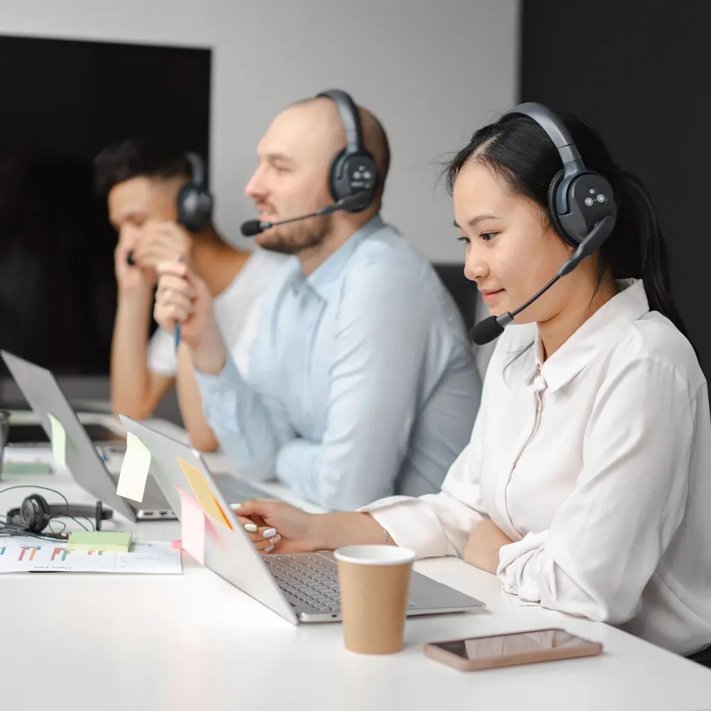 Contact-center staff using headsets and laptops at a shared desk.
