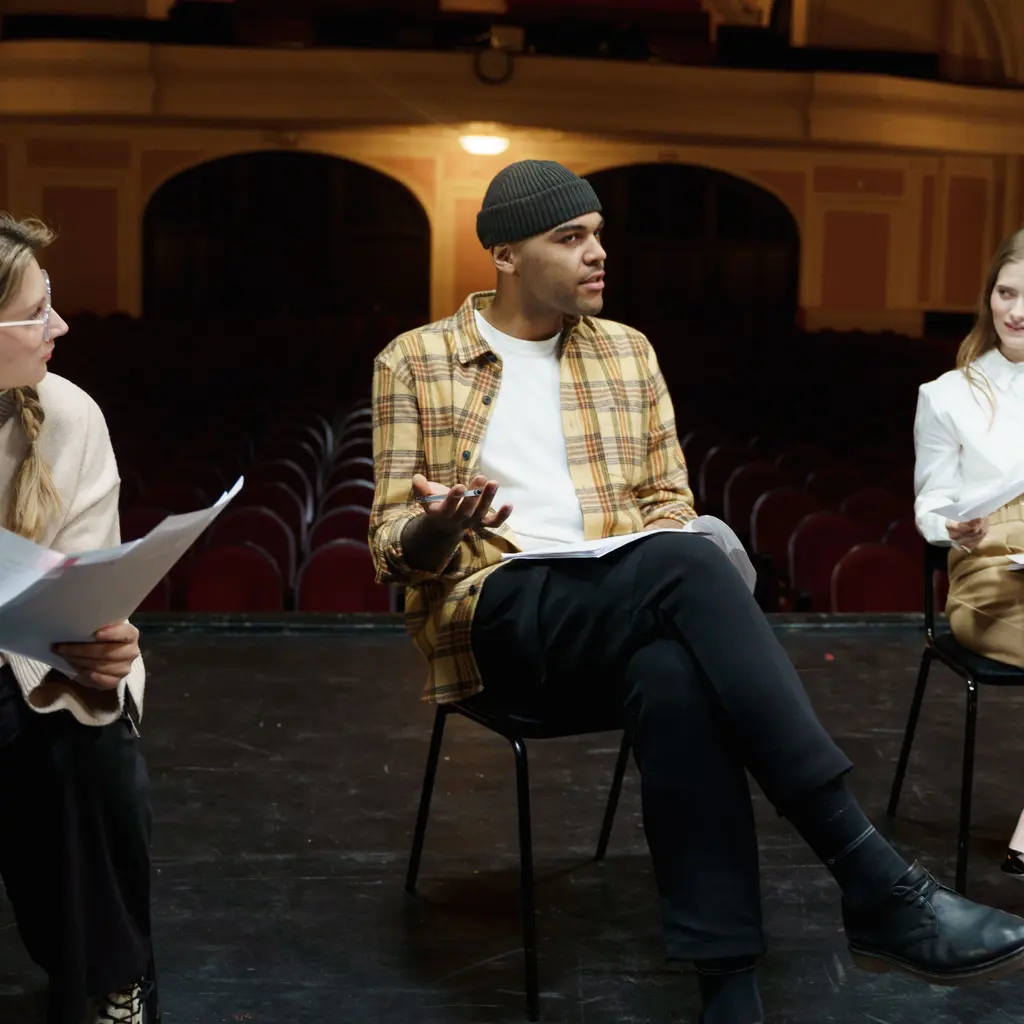 Three performers rehearsing with scripts in a theater.