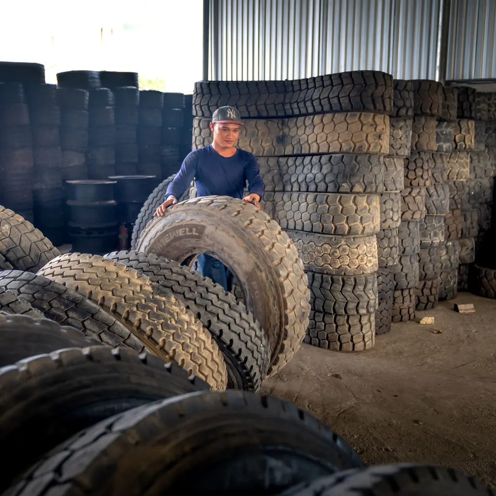 A worker rolling a large truck tire inside a tire warehouse.