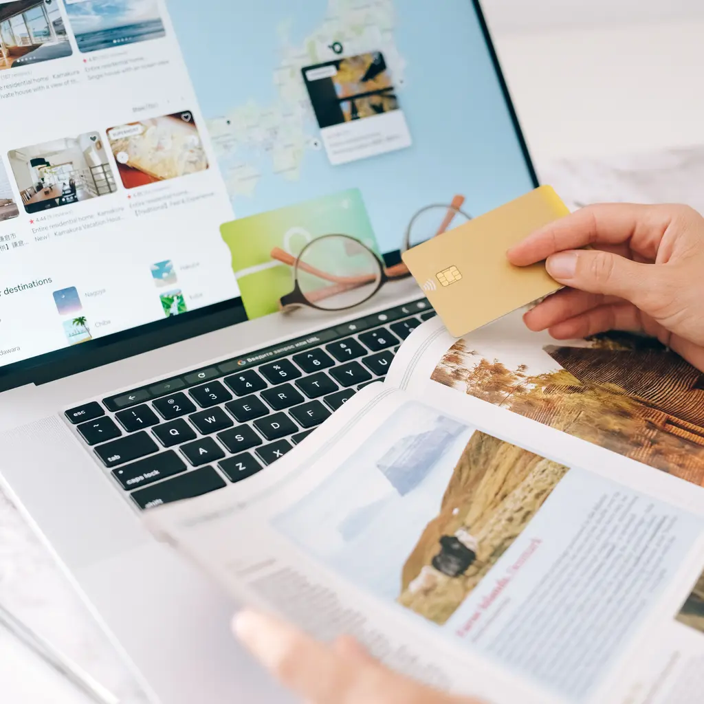 Travel listings on a laptop beside a guidebook and a payment card.