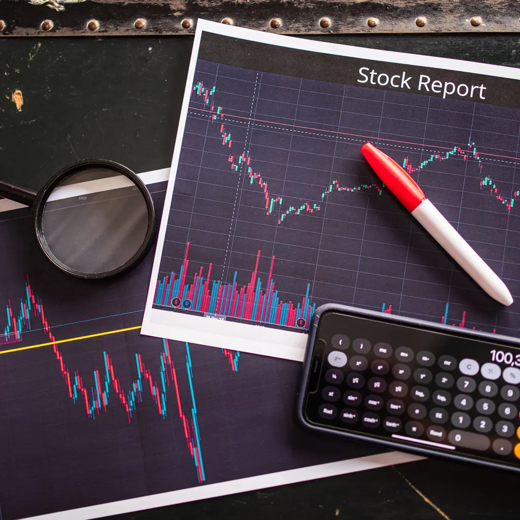 Printed stock-price charts with a calculator, pen and magnifying glass.