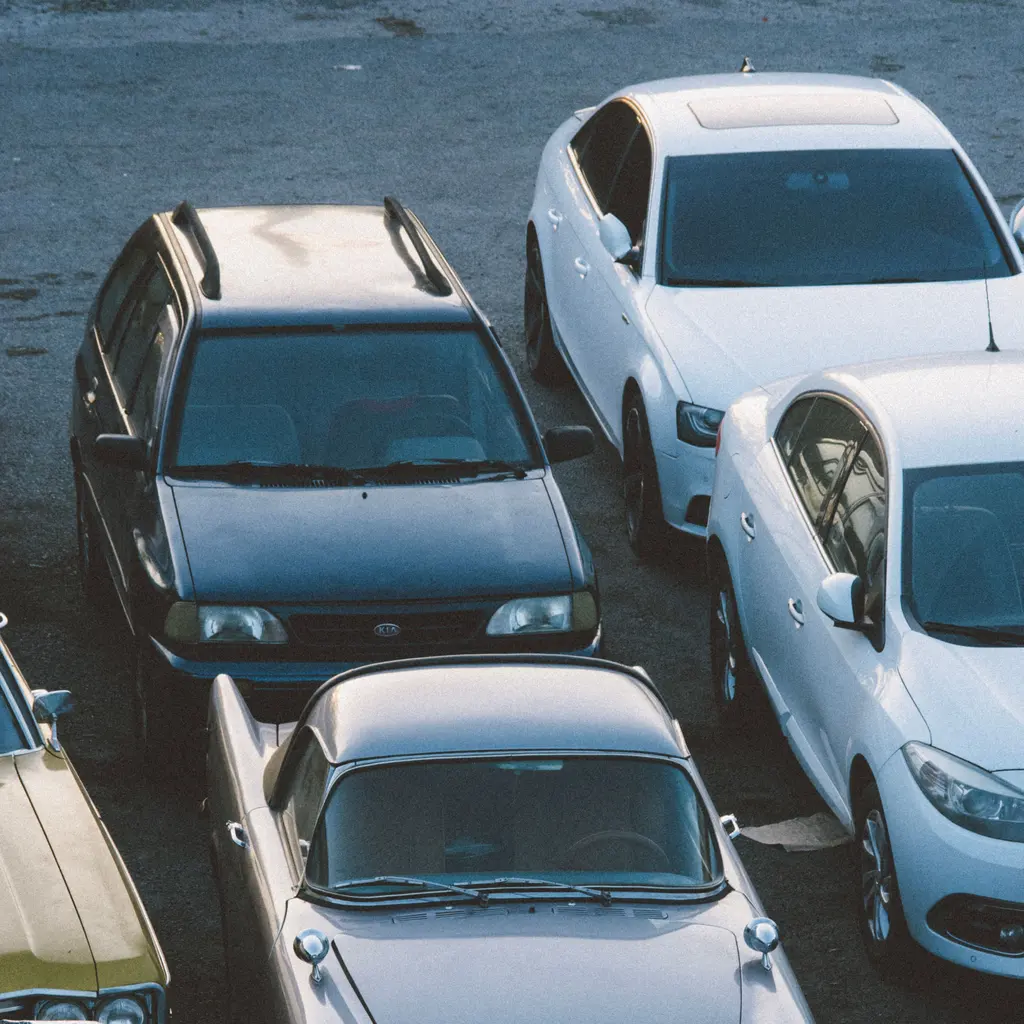 Older and newer passenger cars parked closely together in an outdoor vehicle lot.