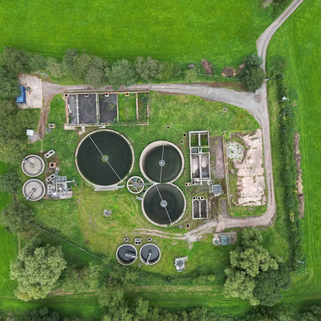 Circular treatment tanks and rectangular basins form a wastewater plant among green fields.