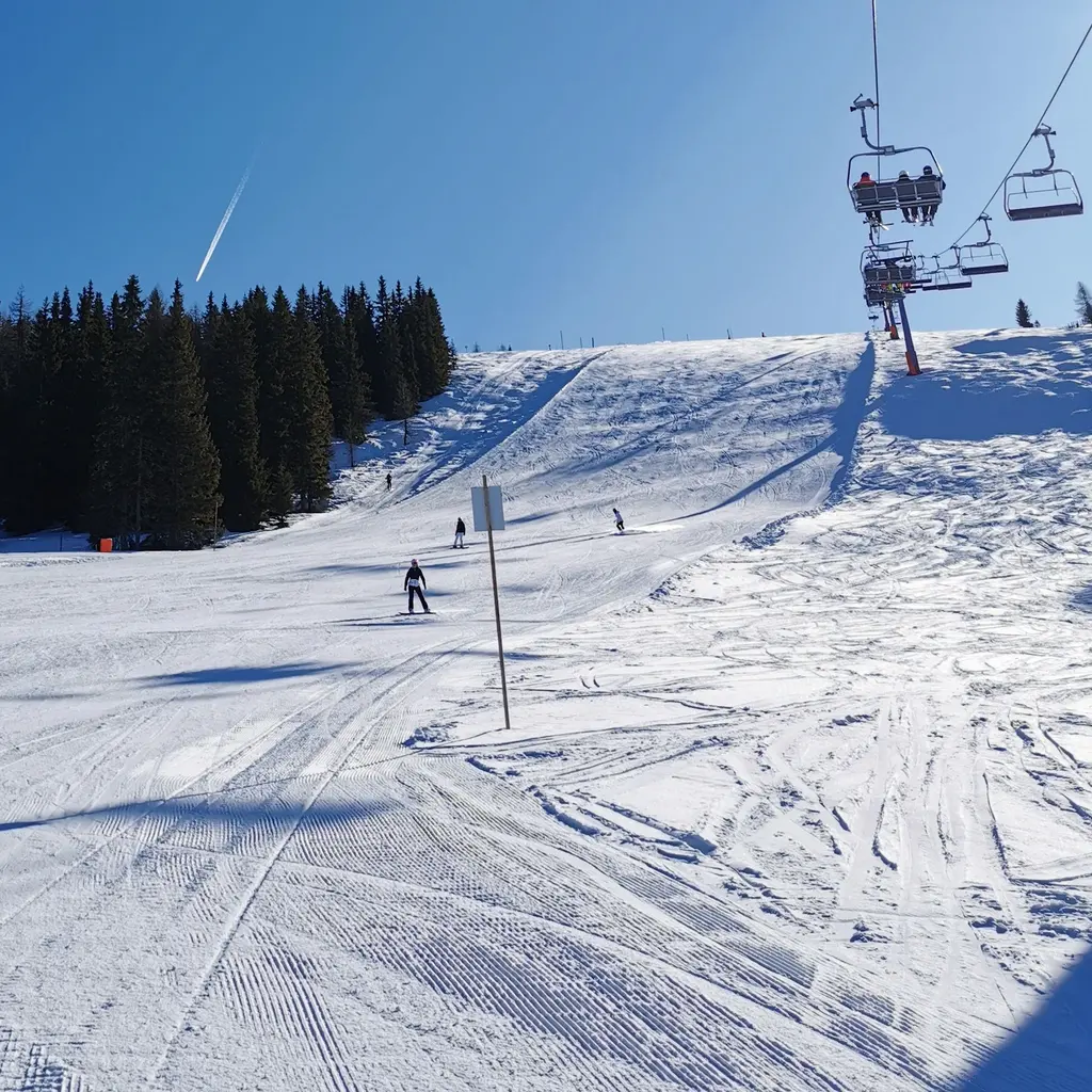 Skiers cross a groomed snowy slope beneath a line of chairlifts.