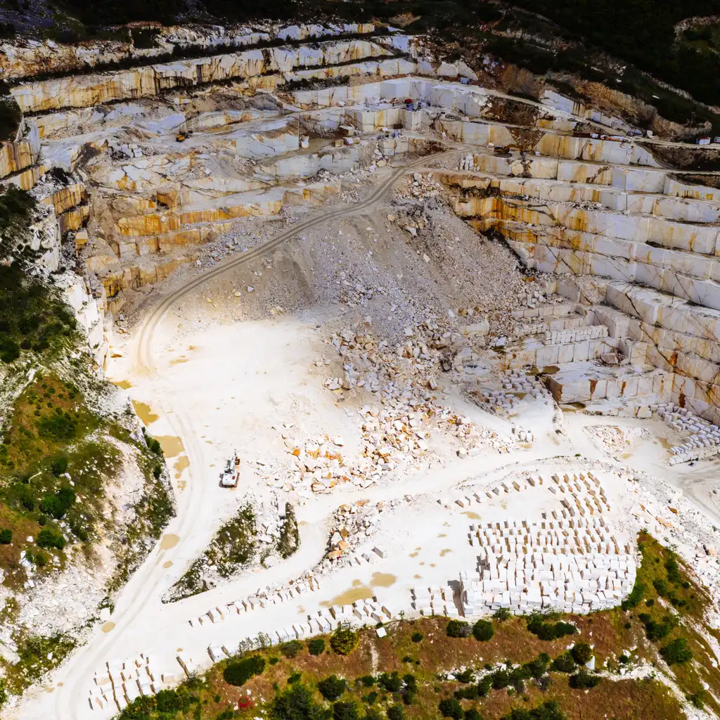 Rows of cut marble blocks sit below stepped quarry faces and access roads.