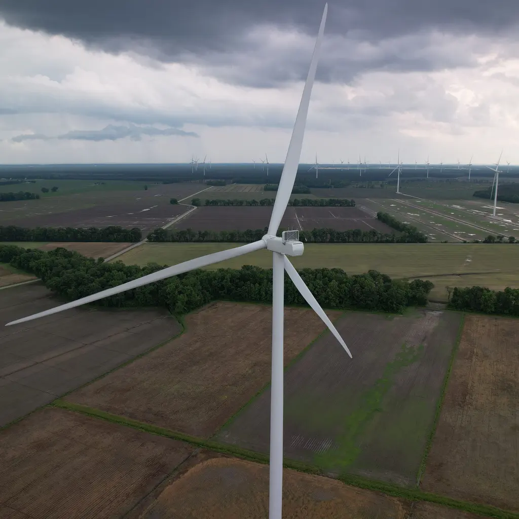 A wind turbine rises above farmland, with more turbines along the horizon.