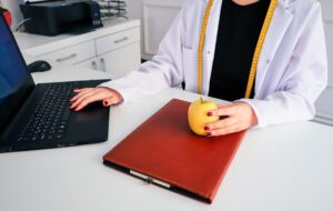 "Doctor with an apple and laptop, exploring HMO insurance: benefits, costs, and coverage."