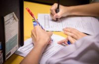 Hands writing on papers, representing inclusive employment and insurance benefits that empower all workers.