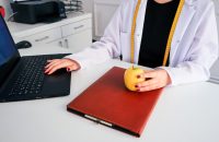 "Doctor with an apple and laptop, exploring HMO insurance: benefits, costs, and coverage."